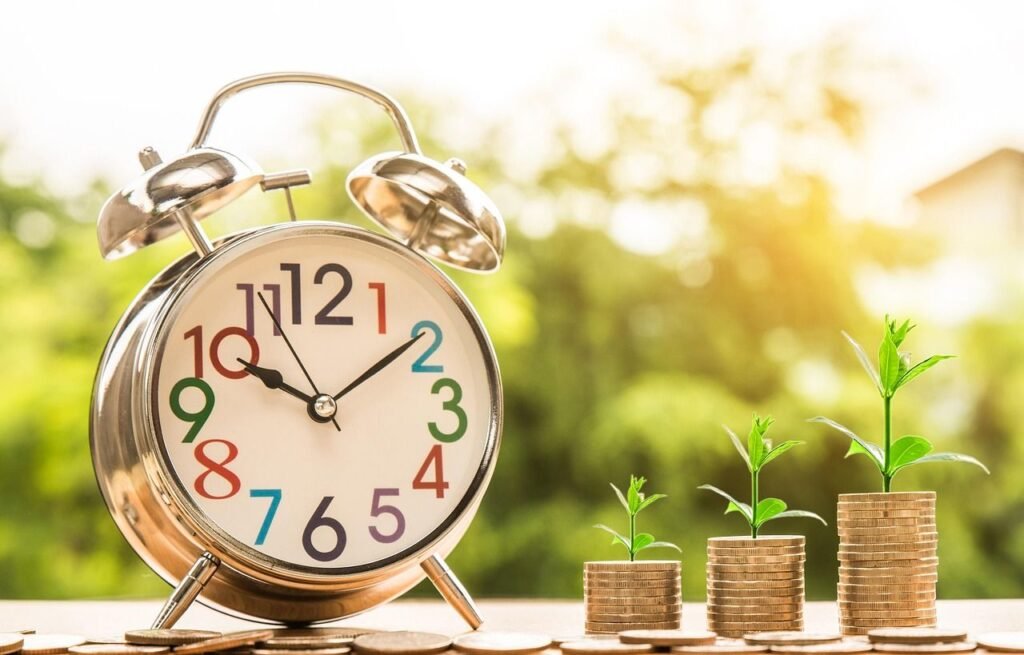 A silver alarm clock beside stacked coins with growing plants, symbolizing the importance of time and investment in term life insurance for future financial security.