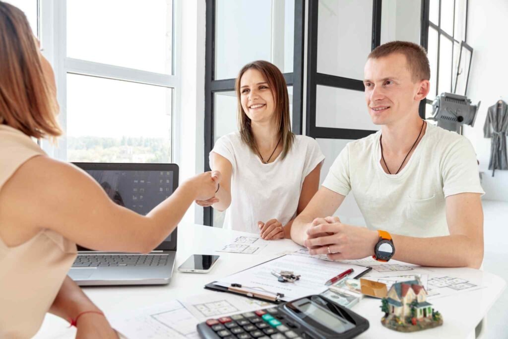 Two individuals (one appearing as an advisor, the other a client) shaking hands across a table in a modern office setting. This conveys trust and professional guidance.